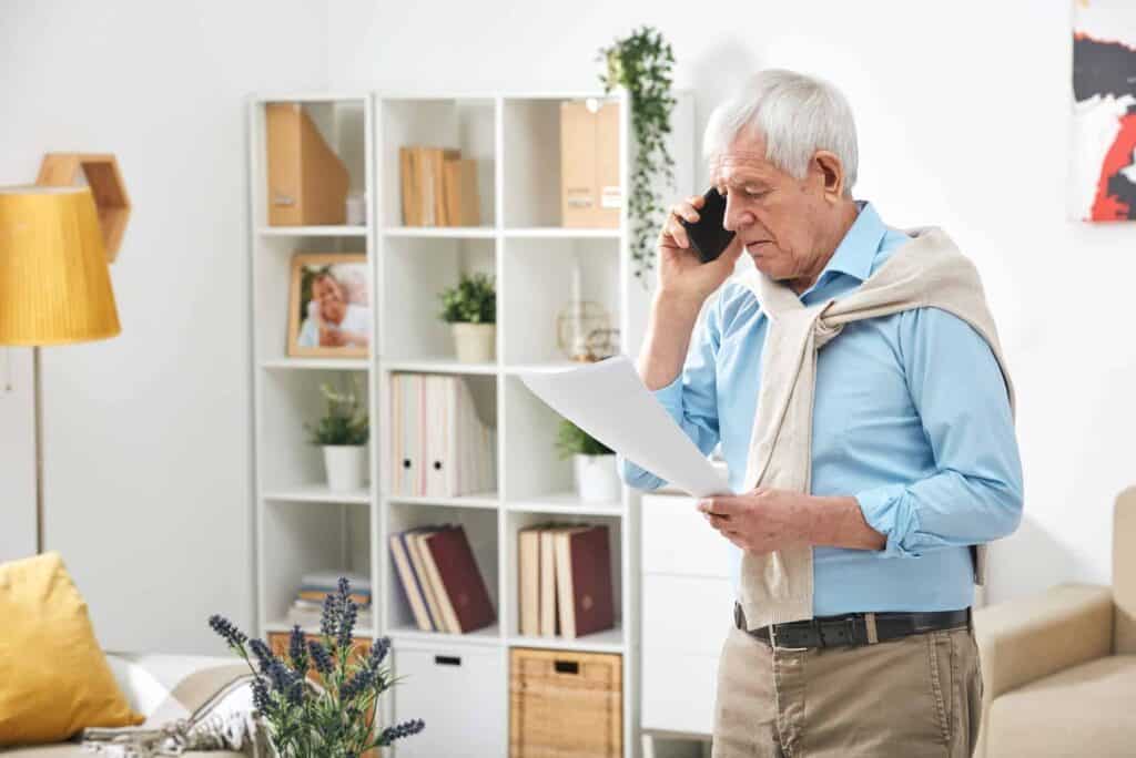 A senior looking at a document with a phone on his ear. We offer counseling services to all ages.